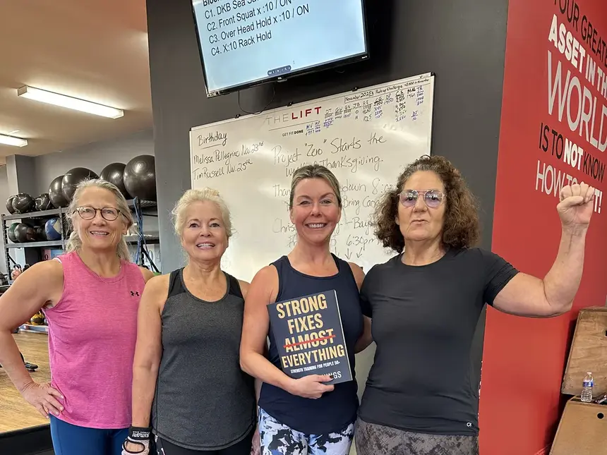 Four members in front of the whiteboard, one holding a copy of Strong Fixes Almost Everything