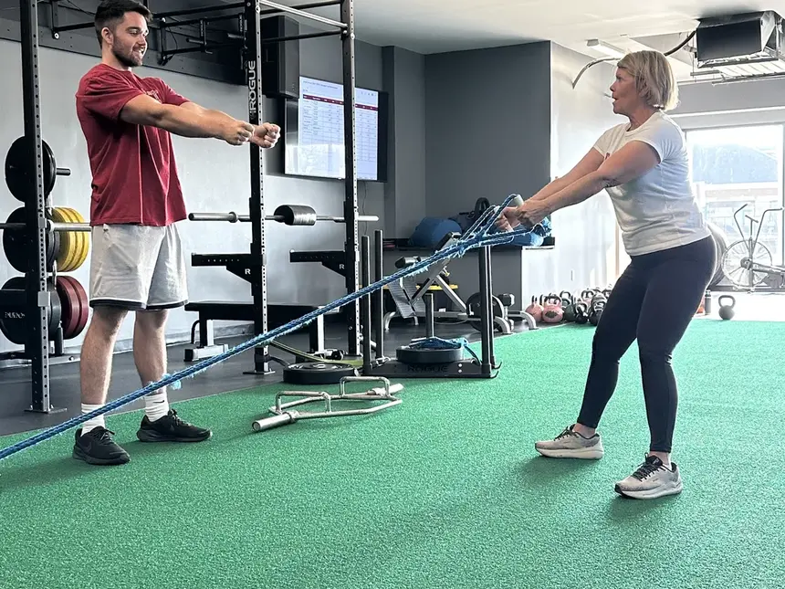 A coach anchoring a resistance band while a member rows it across the green turf